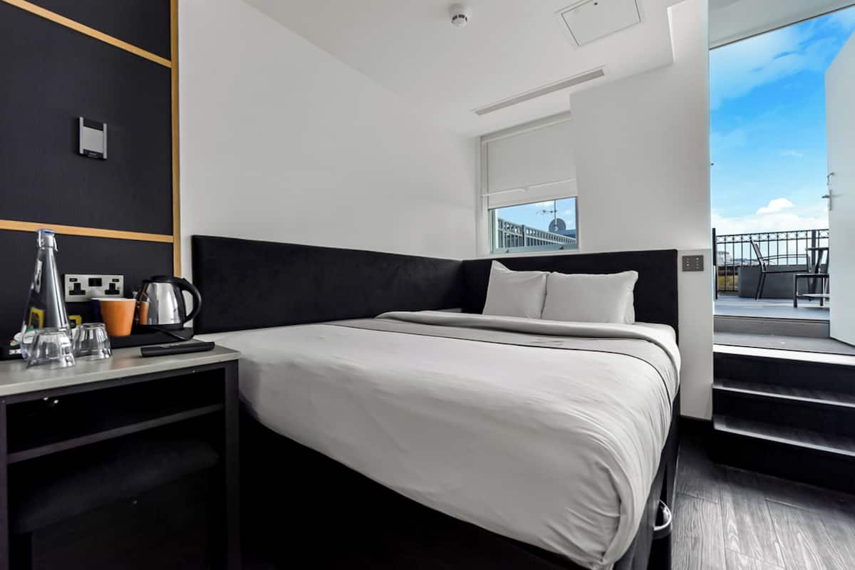 Una habitación de hotel moderna con una cama grande, un escritorio con hervidor y vistas a la ciudad a través de una ventana.