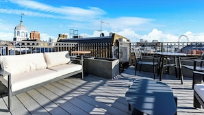Una terrazza sul tetto con divano, tavolo da pranzo e sedie, con vista su un panorama urbano caratterizzato da architetture uniche e una ruota panoramica.