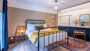 A hotel room with a bed, a desk, a mirror, and a window with curtains.