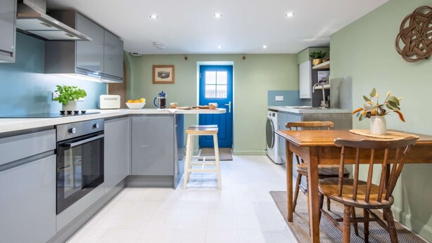A modern kitchen with grey cabinets, a blue door, and a dining area with wooden chairs and a table.