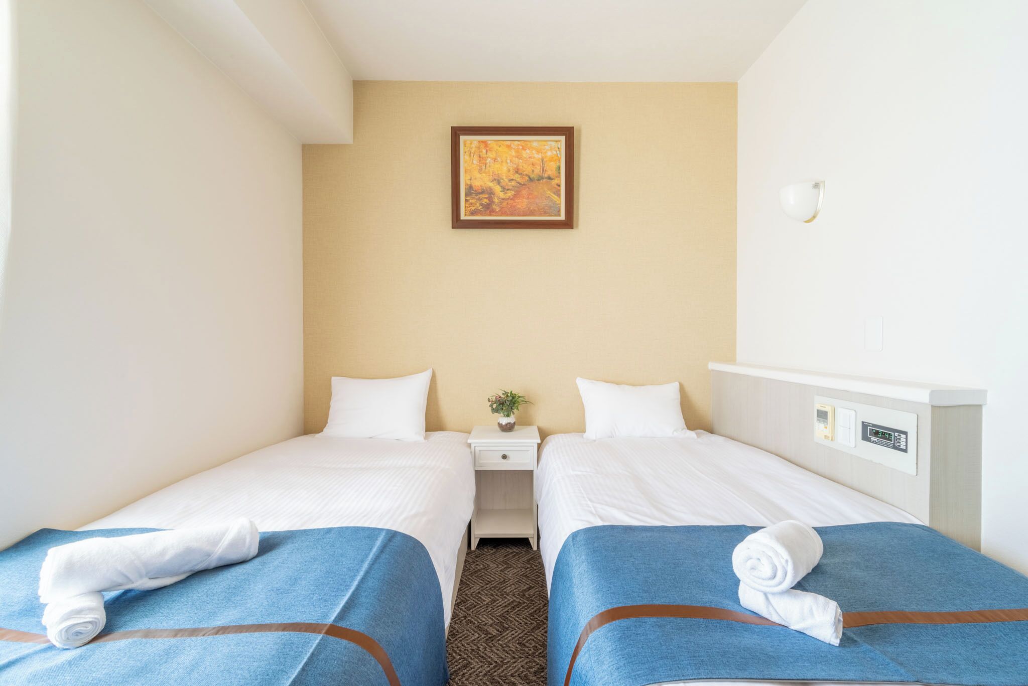 Une chambre d’hôtel avec deux lits, une table de chevet, un tableau au mur et une petite plante.