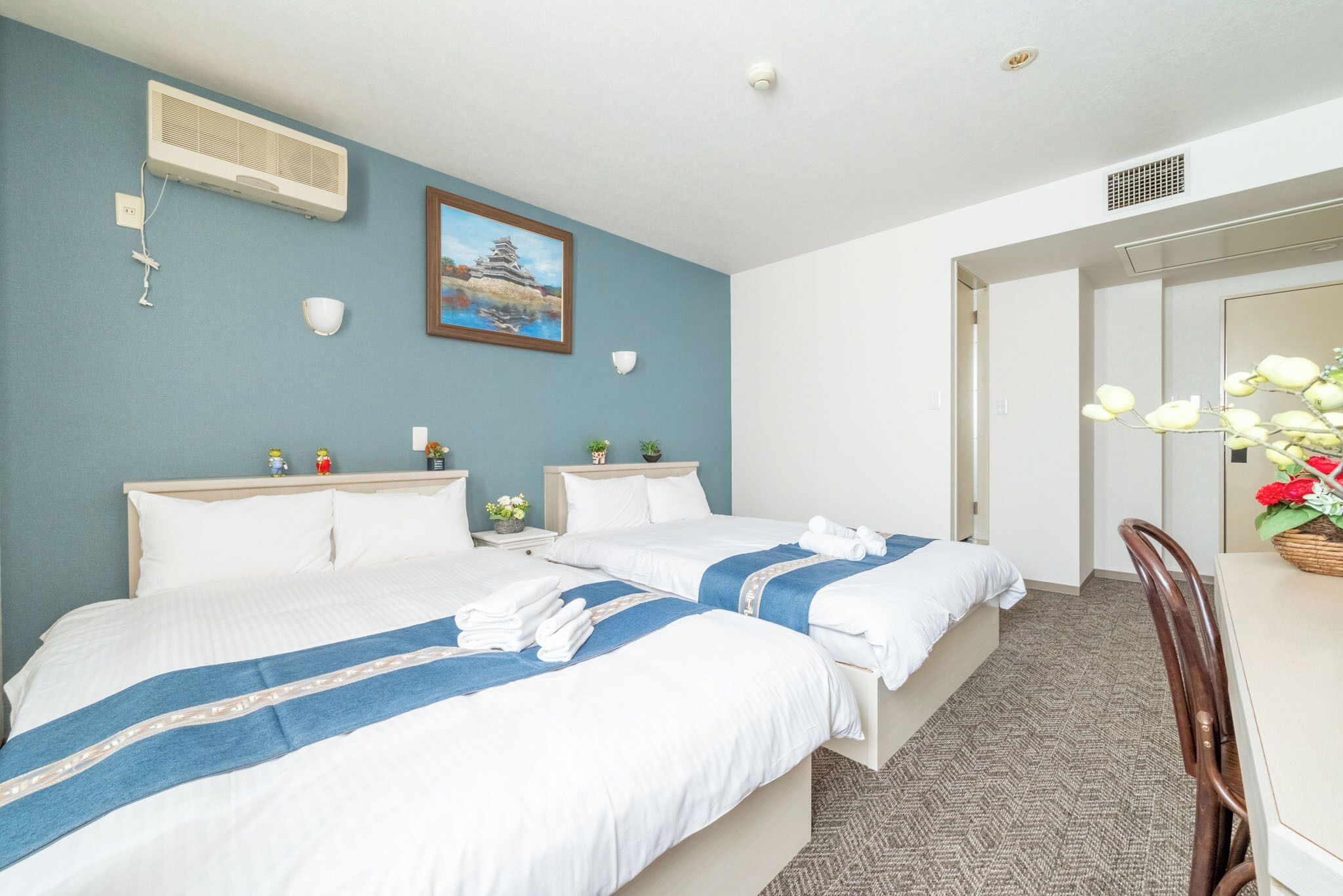 A hotel room with two beds, a large mirror, a dining table with chairs, and a painting on the wall.
