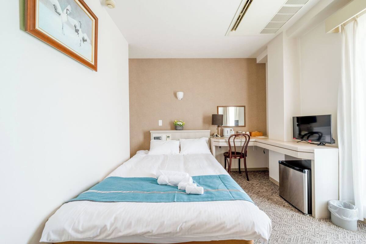 Une chambre d’hôtel équipée d’un lit, d’un bureau, d’une chaise, d’une télévision et d’une petite poubelle.