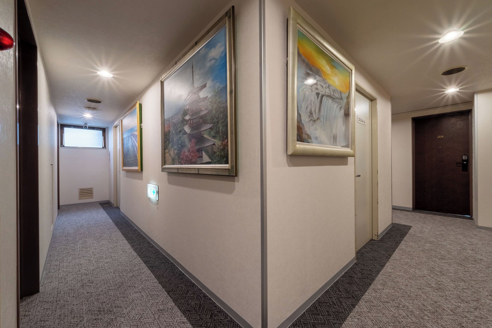 A hallway with framed artwork on the walls, a carpeted floor, and a door labeled "2014" at the end.