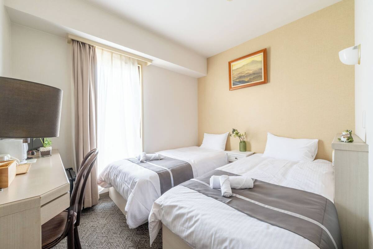Une chambre d’hôtel avec deux lits, un bureau, une chaise, une télévision et un tableau au mur.