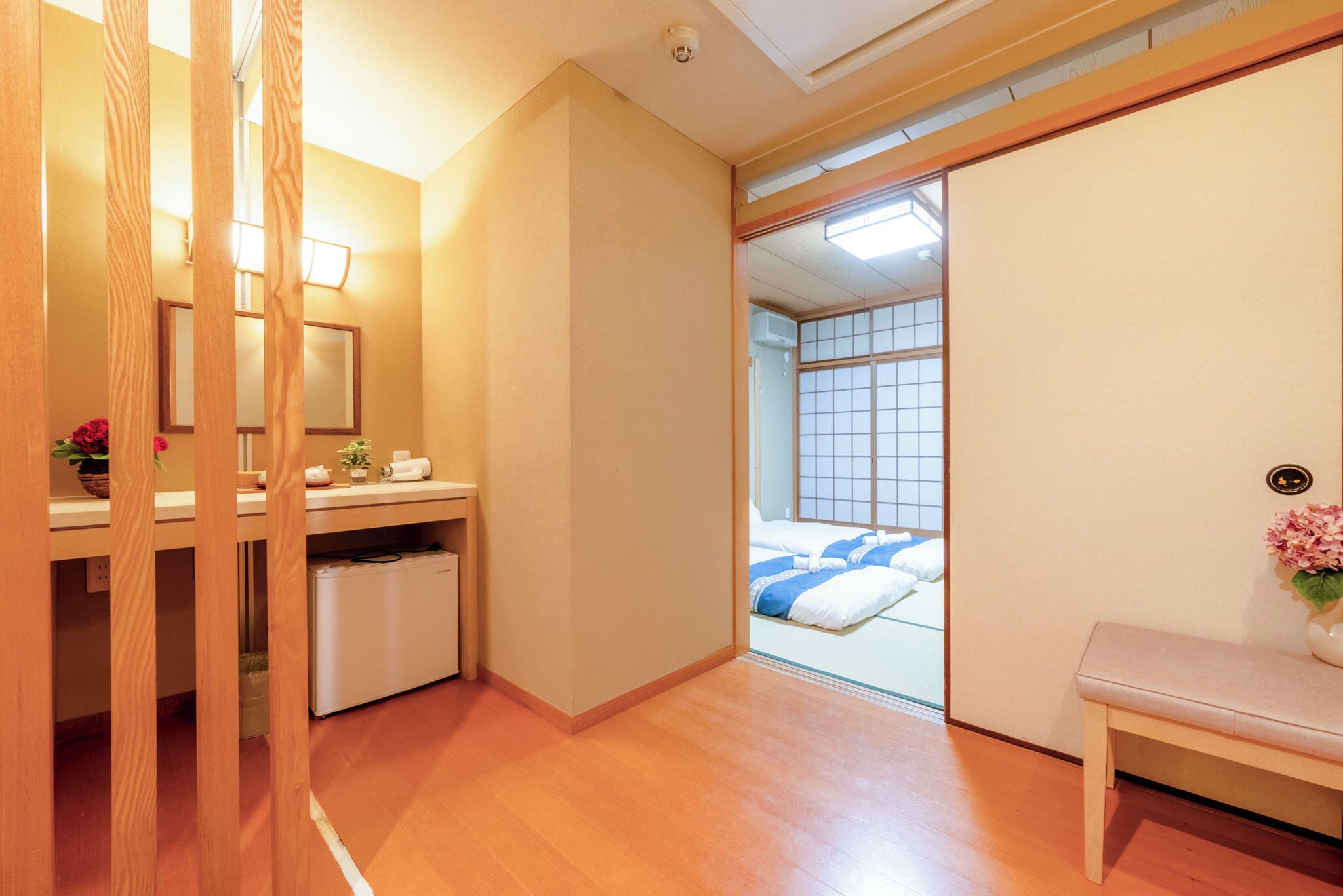 A traditional Japanese room with a wooden floor, a bed with blue bedding, a small bedside table, and a wooden partition.