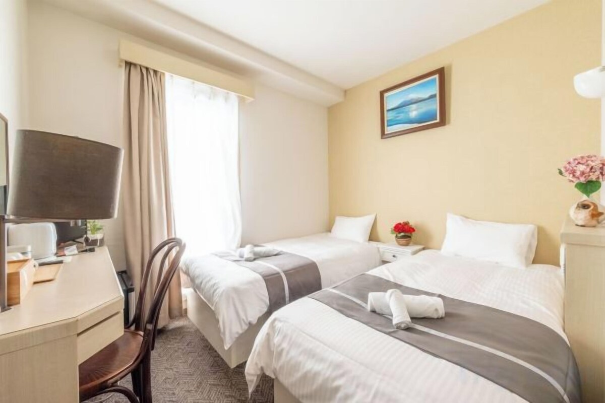 Habitación de hotel con dos camas, un escritorio, una silla, un televisor y una ventana con cortinas.