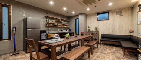 Cocina compacta con refrigerador, estufa y repisas de madera. Hay una mesa con bancos y un sofá negro.
