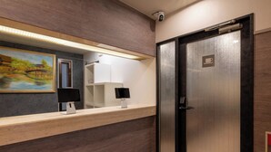 A modern reception area with a wooden counter, a painting of a bridge, a security camera, and a door with a coffee symbol.