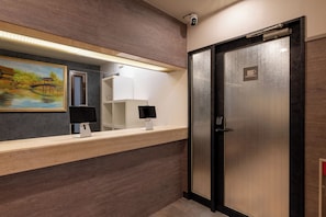 Una moderna zona de recepción con mostrador de madera, un cuadro de un puente, una cámara de seguridad y una puerta con el símbolo de una taza de café.