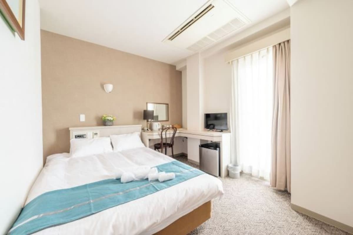 Une chambre d’hôtel avec un lit, un bureau, une télévision et une fenêtre avec des rideaux.