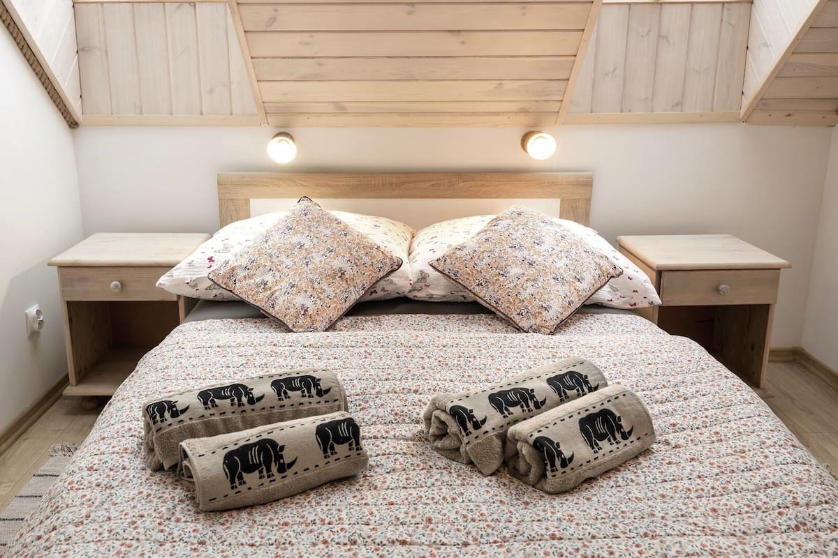 Un dormitorio con cabecera de madera, dos mesitas de noche, colcha con estampado floral y múltiples toallas con diseños de animales.