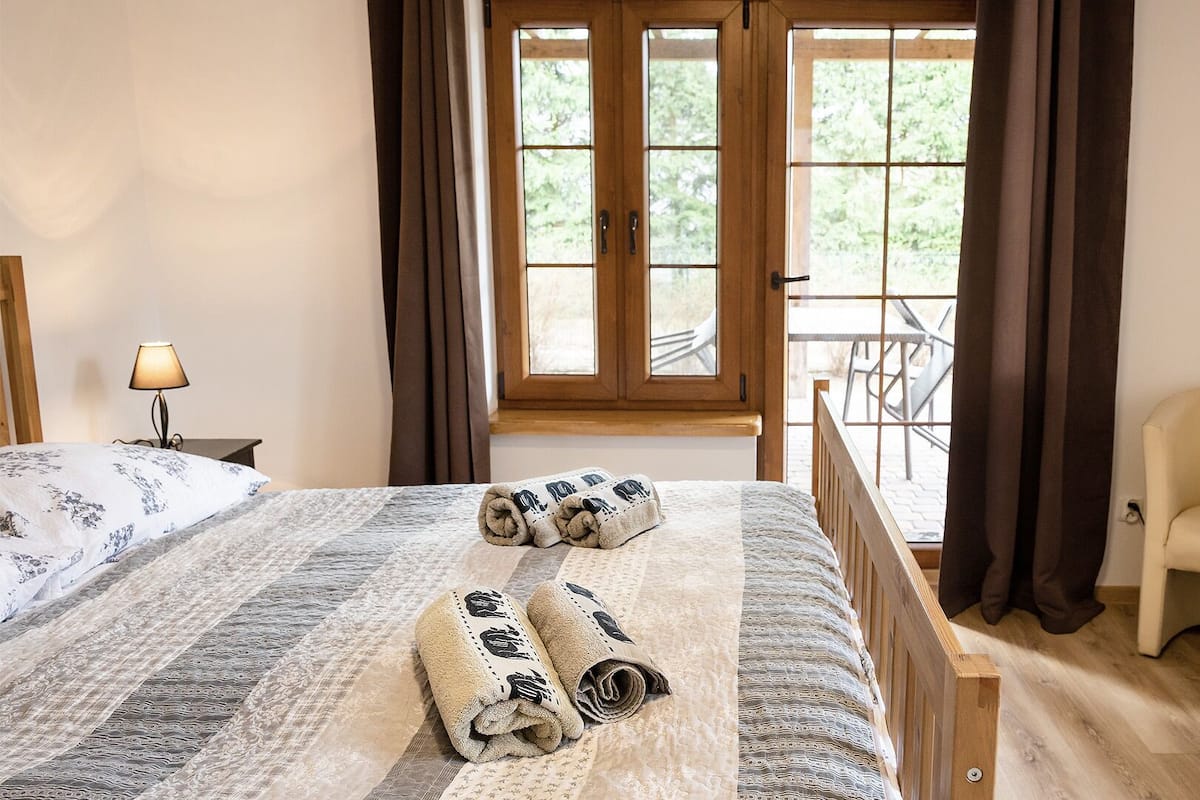 Un dormitorio con cama, una silla, una lámpara y vistas al exterior a través de una ventana.
