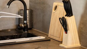Una cocina moderna con armarios de madera, un grifo negro, una estufa integrada y una tabla de cortar de madera con un frutero para cuchillos.
