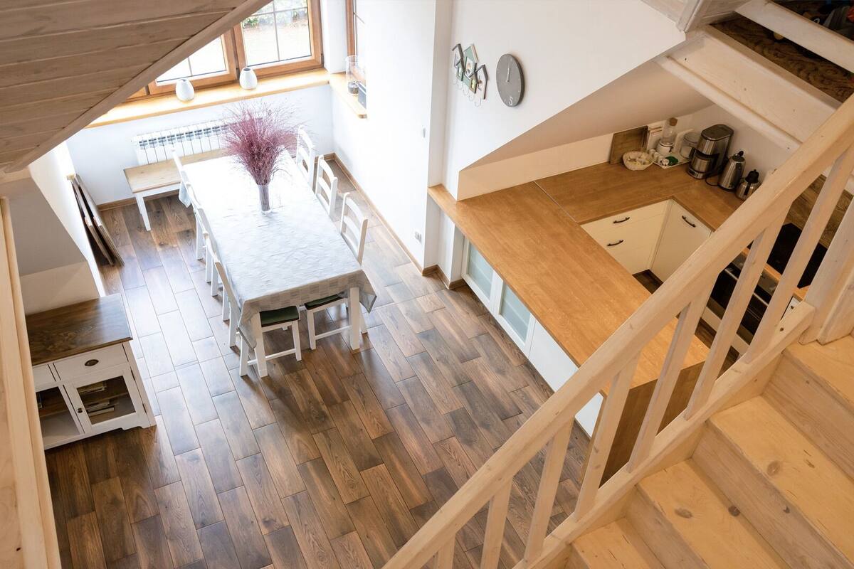 Una cocina amplia con suelo de madera, un comedor con mesa y sillas, y una escalera que lleva a un nivel superior.