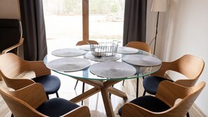 Una mesa redonda de vidrio con seis sillas, cada una con un mantel tejido, en una habitación con vista a una obra en construcción.