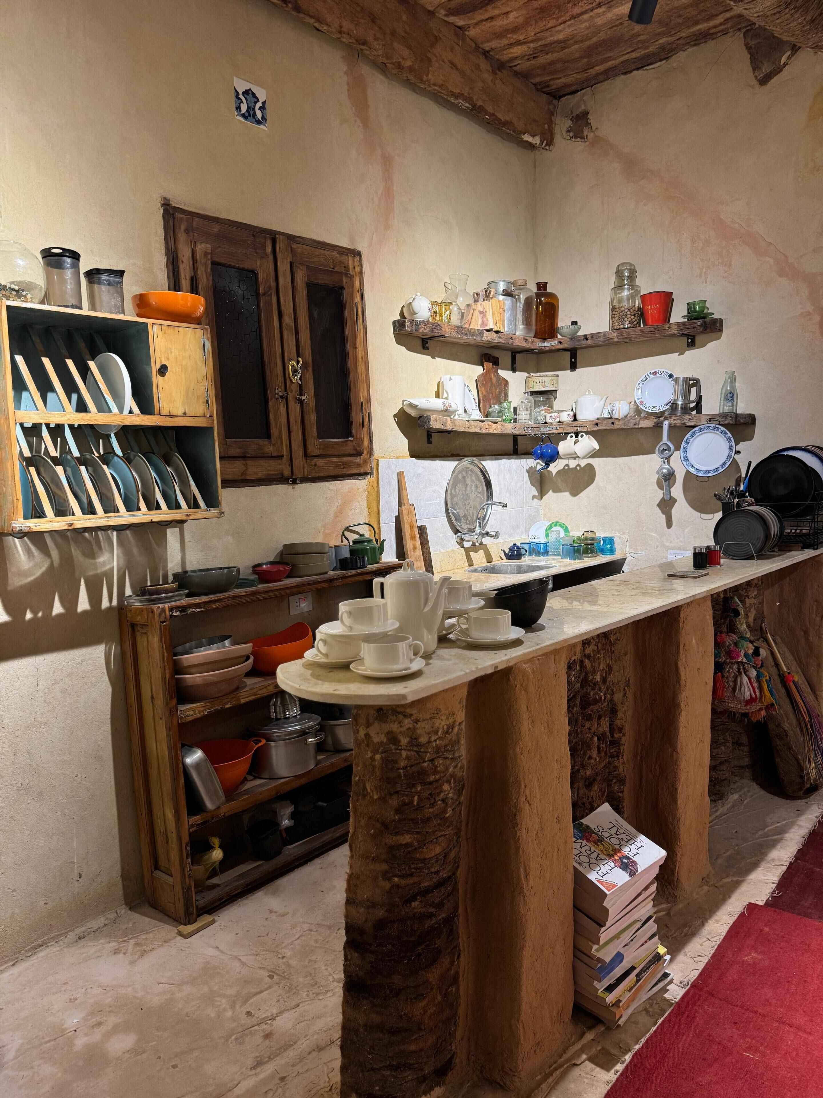A rustic kitchen with wooden cabinets, shelves with dishes, and a central island with kitchenware.
