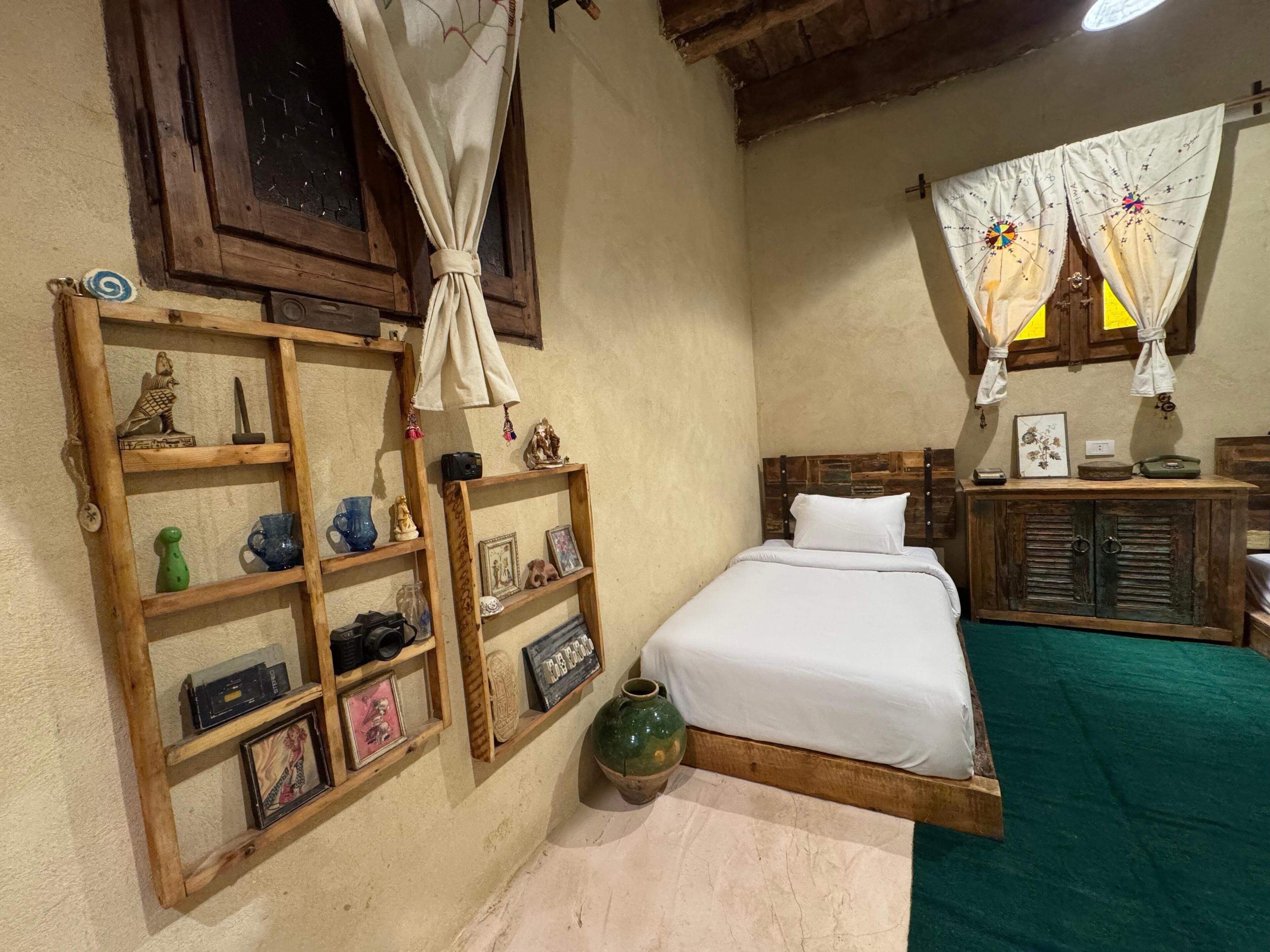 Een slaapkamer met een houten bed, een plank met diverse spullen, een groen vloerkleed en een rustiek houten hoofdeinde.