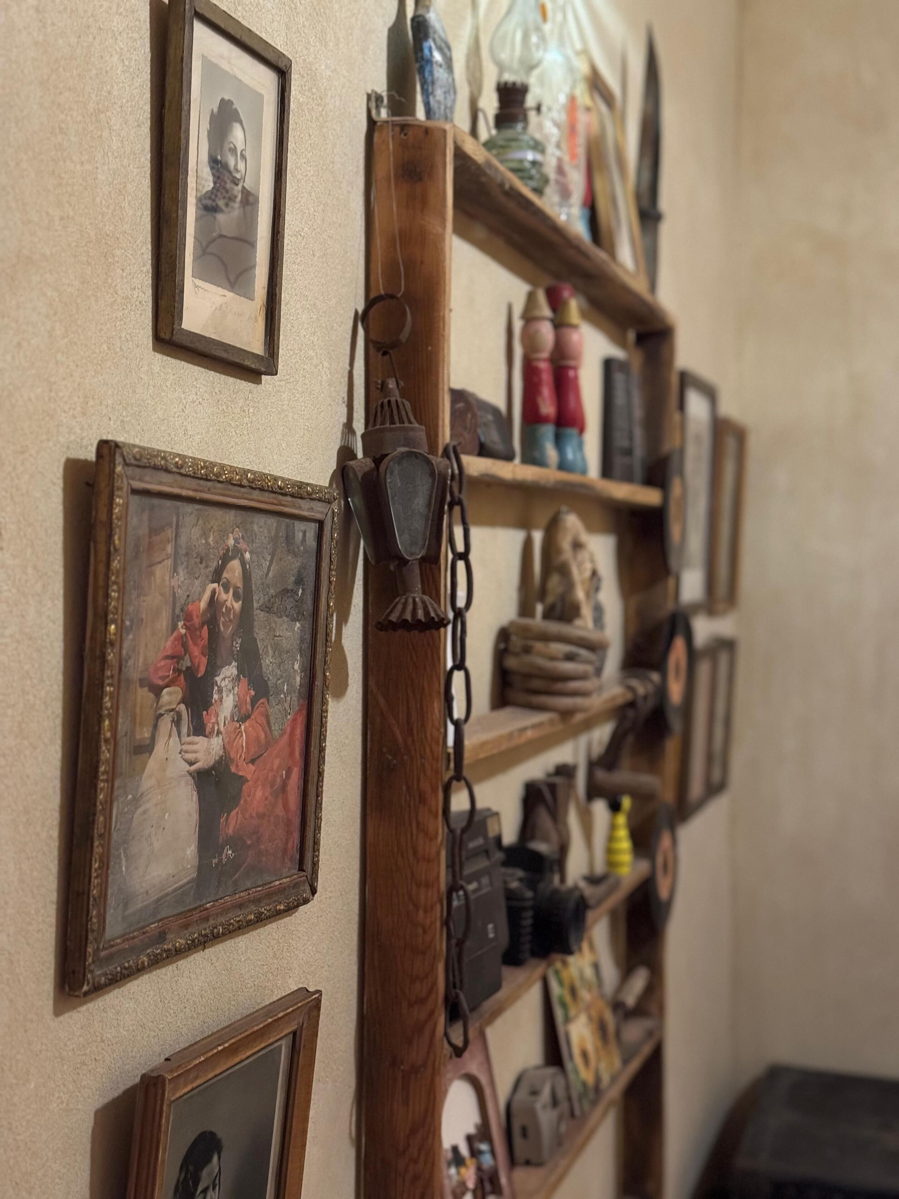 A wall with various framed pictures and a wooden shelf holding items like bottles and a lantern.