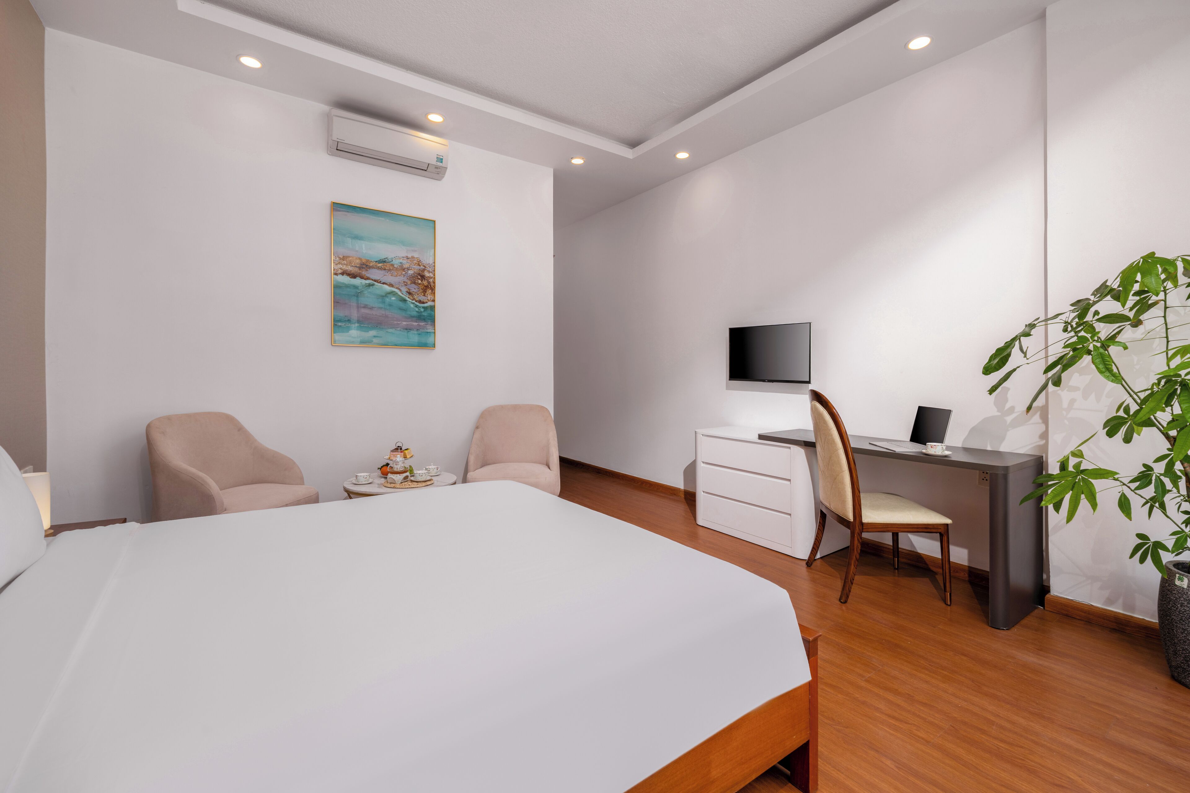 Ein Hotelzimmer mit einem großen Bett, zwei Sesseln, einem Schreibtisch mit Computer, einem Fernseher und einer Pflanze.