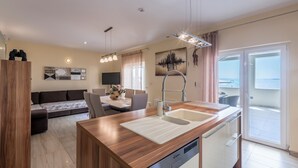 A modern kitchen with a built-in dishwasher, a dining area with a table and chairs, a sofa, and a large window with a view. - VILLA MARCO In front of sea (Okrug Gornji)