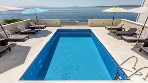 A rooftop swimming pool with lounge chairs and umbrellas, overlooking a body of water. - VILLA MARCO In front of sea (Okrug Gornji)