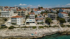 A coastal residential area with multi-story buildings, clear turquoise waters, and rocky terrain. - VILLA MARCO In front of sea (Okrug Gornji)