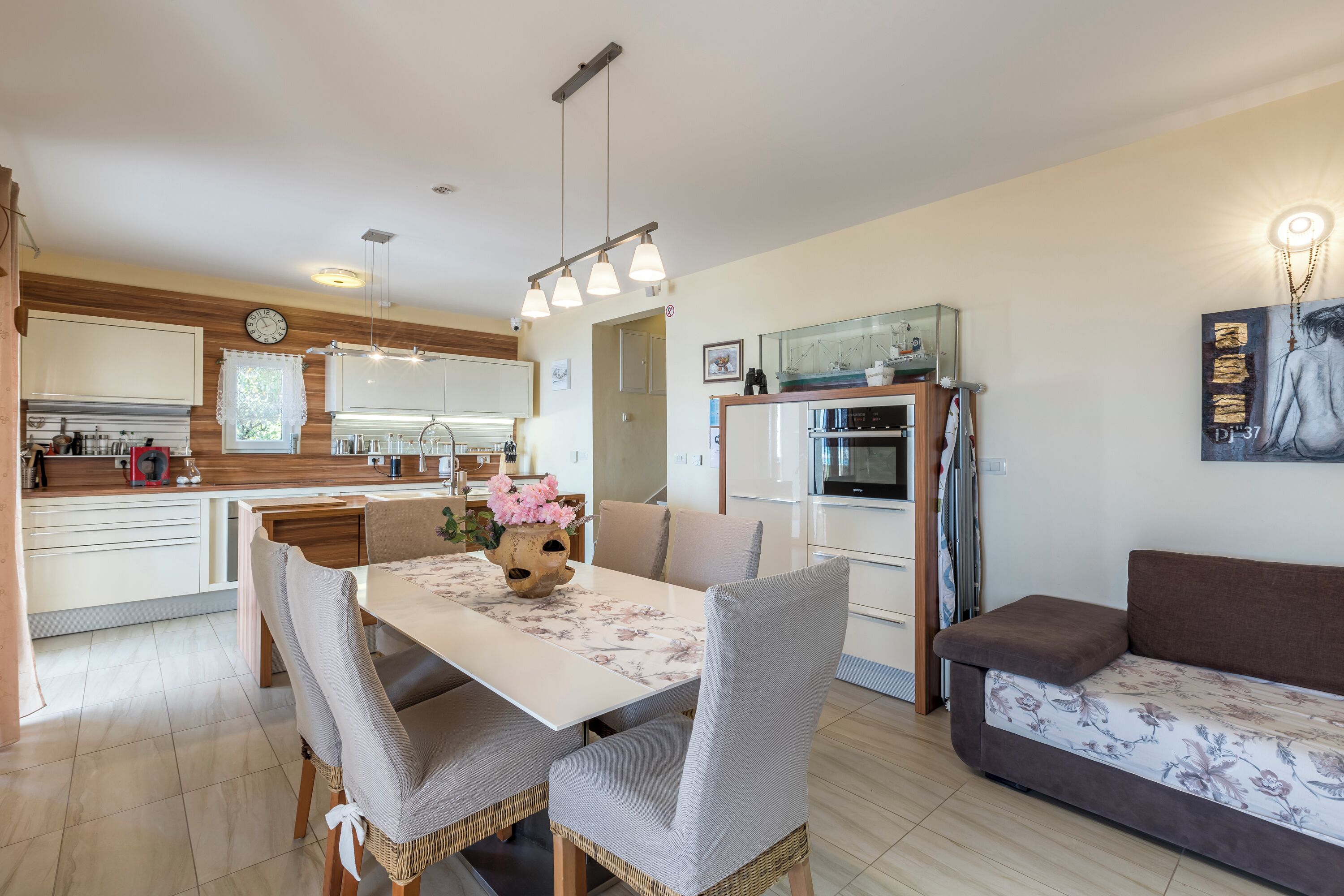 A modern kitchen with white cabinets, a dining table with chairs, and a sofa.