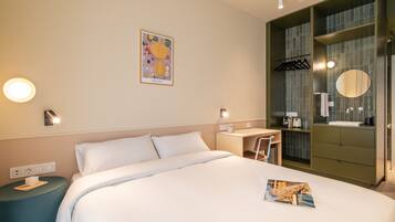 Habitación de hotel con cama, mesita de noche, escritorio y baño con espejo y lavamanos.