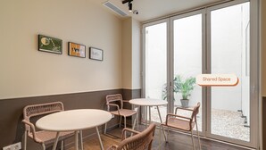 A shared space with wicker chairs and a round table, large windows, and artwork on the wall.