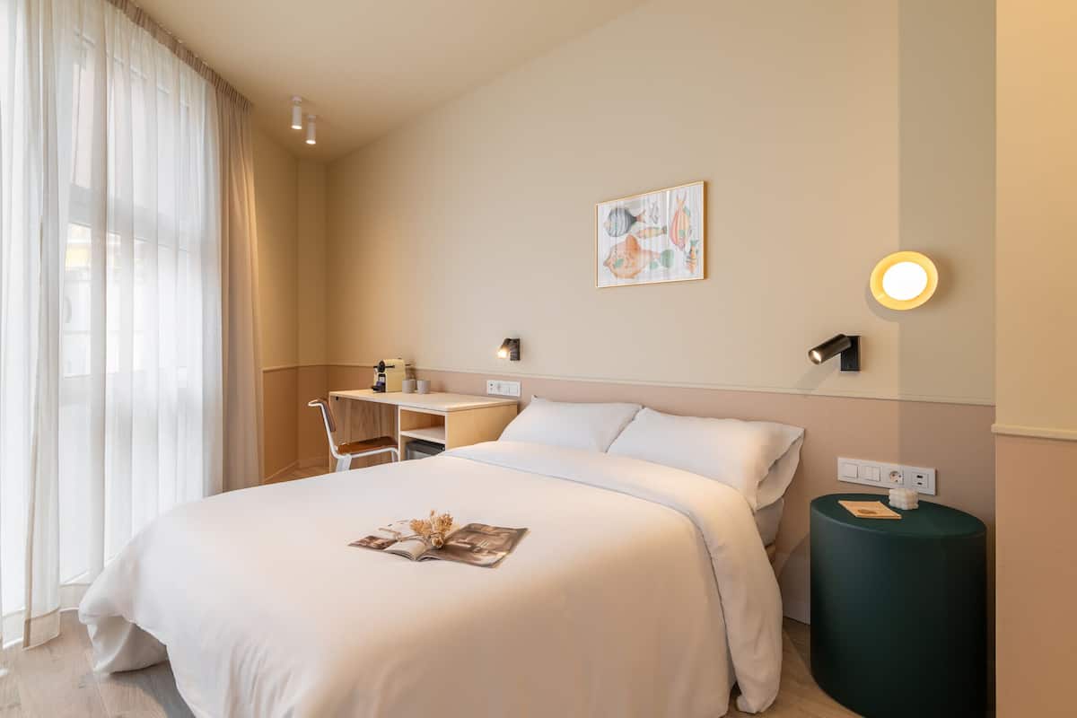 Hotelkamer met een bed, bureau, stoel, klein tafeltje en een wandlamp.