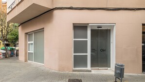 A building with a beige exterior, a glass door entrance, and a trash bin on the sidewalk.