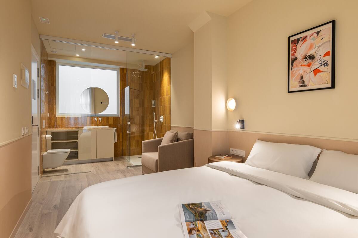 Een hotelkamer met een groot bed, een bureau, een stoel, een douche met glazen wanden, en een kunstwerk aan de muur.