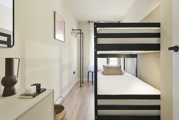 A bunk bed with a black frame and white bedding, a small desk with a lamp, and a framed picture on the wall.