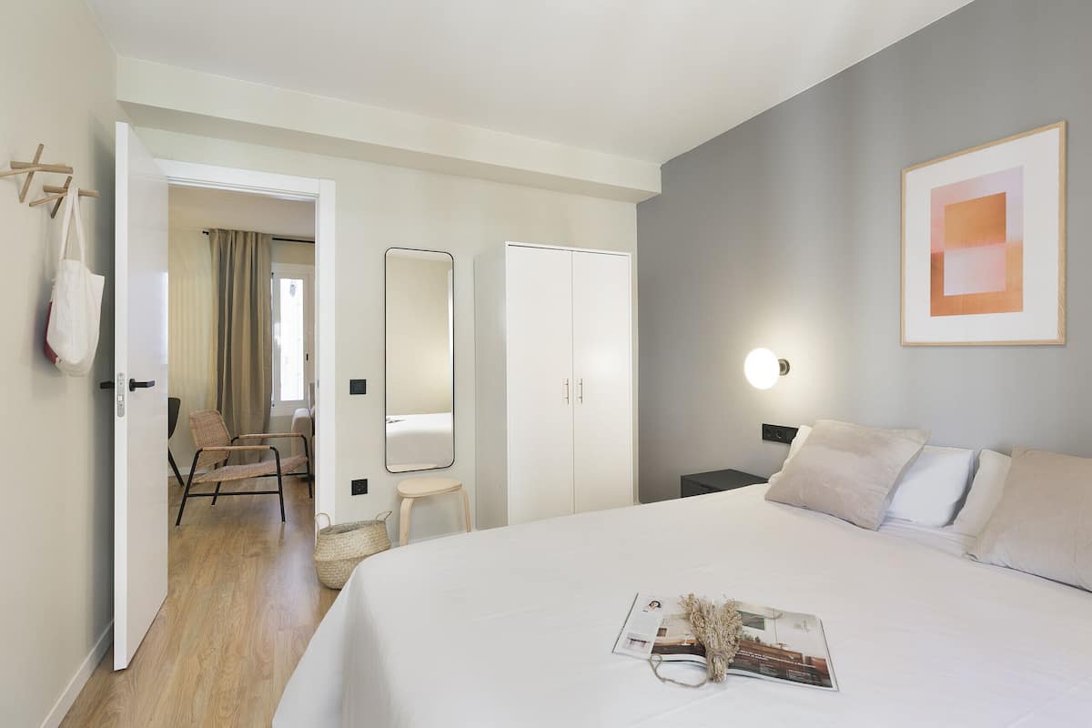 A hotel room with a large bed, a bedside table, a chair, a wardrobe, and a mirror.