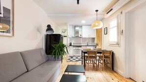 Un salon moderne avec un canapé gris, une table à manger avec des chaises, et une cuisine en arrière-plan.