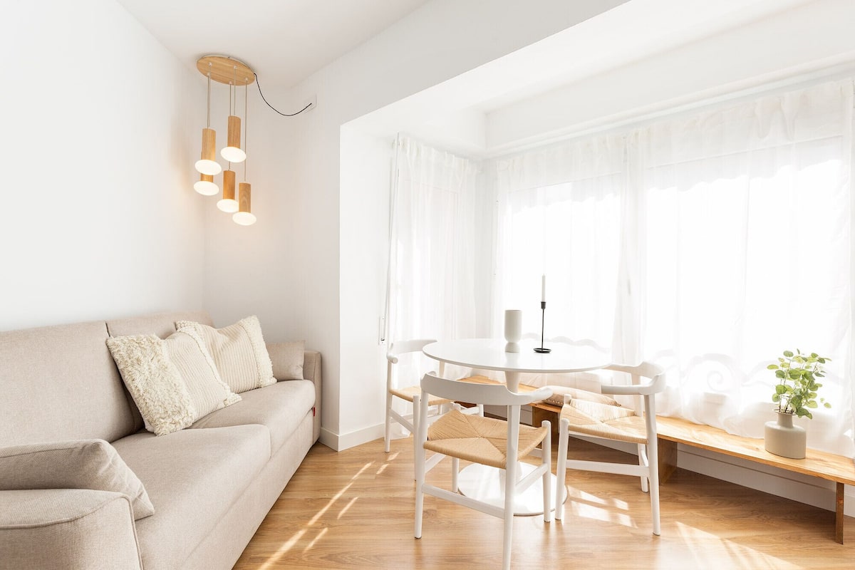A modern living room with a beige sofa, a round white table, and a bench.