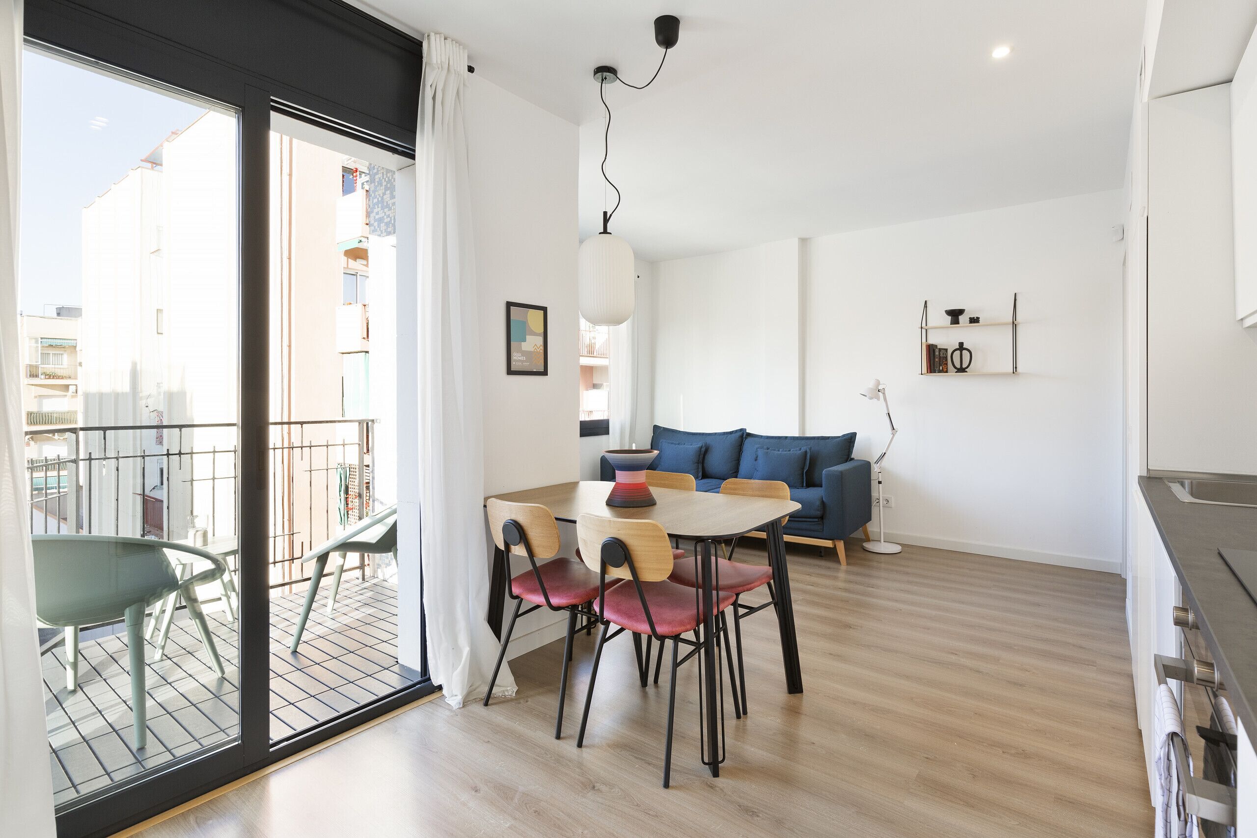 Una sala moderna con comedor, un sofá y un balcón con vistas a edificios.