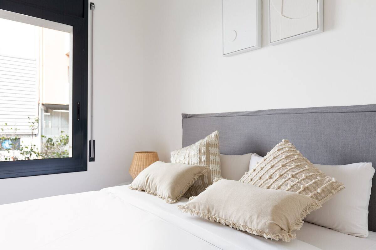 Un dormitorio con cama, almohadas, una lámpara y una ventana.