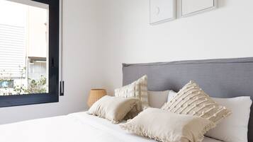 Un dormitorio con cama, almohadas, una lámpara y una ventana.