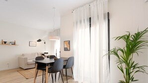 Un salon moderne avec un coin repas, comprenant un canapé, une table à manger avec des chaises, une plante en pot et une grande fenêtre agrémentée de rideaux légers.