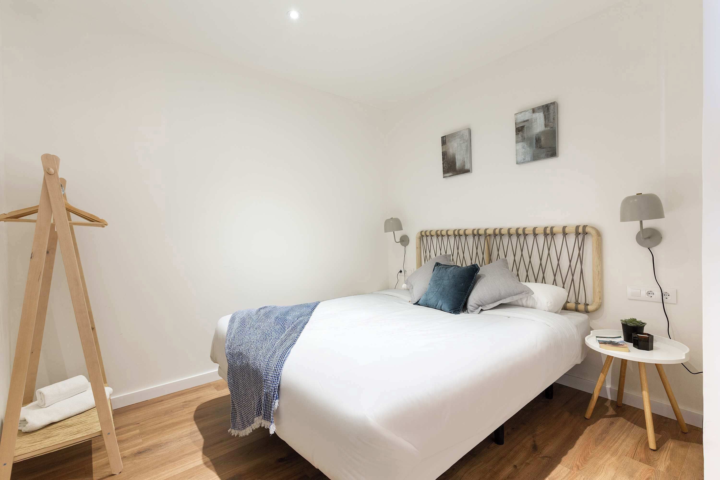 Une chambre à coucher bien rangée, avec un lit, des lampes de chevet, une petite table sur laquelle est posée une plante, et un porte-manteau en bois.