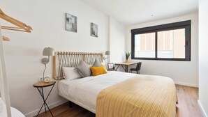 Une chambre à coucher avec un lit, des tables de chevet, une fenêtre et un petit bureau.