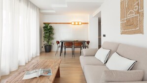 A modern living room with a sofa, a coffee table, and a dining area with a table and chairs. - Port Forum Apartments By Olala Homes (Sant Adria de Besos)