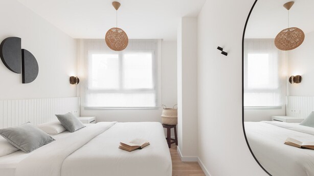 A modern bedroom with a large mirror, two beds, a bedside table, and a window with natural light. - Port Forum Apartments By Olala Homes (Sant Adria de Besos)