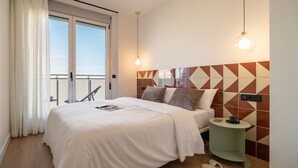 A hotel room with a large bed, a small side table, a view of the outdoors, and a geometric-patterned wall. - Port Forum Apartments By Olala Homes (Sant Adria de Besos)