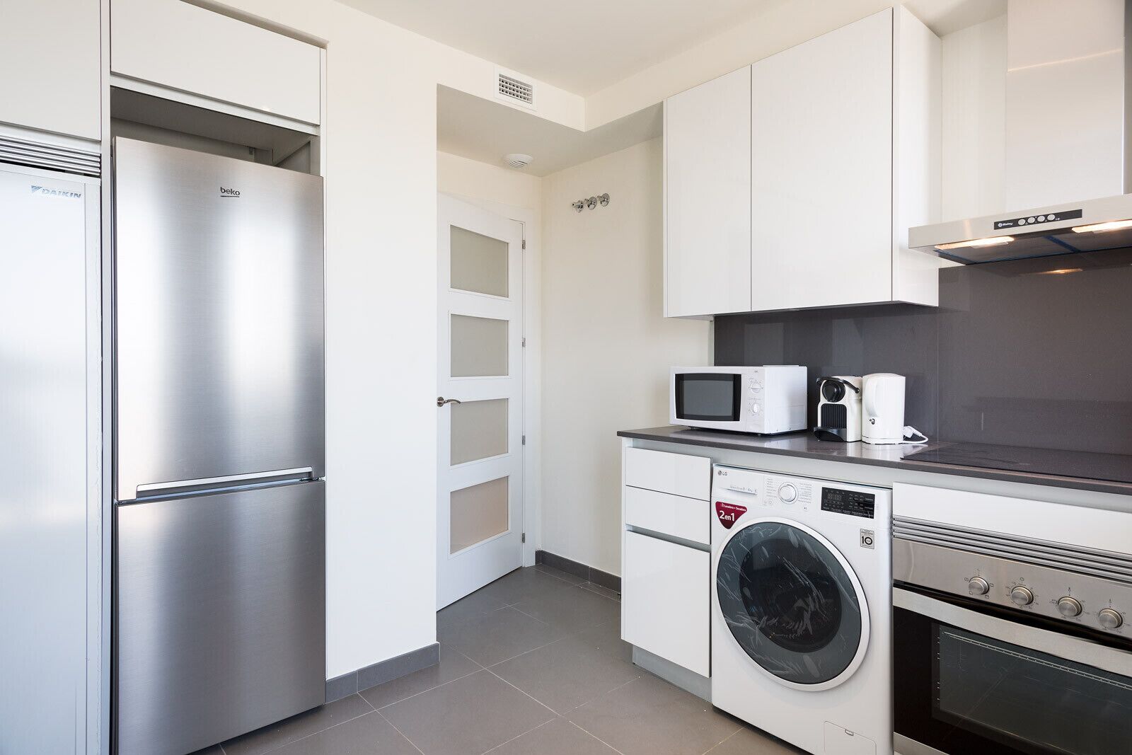 A modern kitchen with a stainless steel refrigerator, a microwave, a washing machine, and an oven.