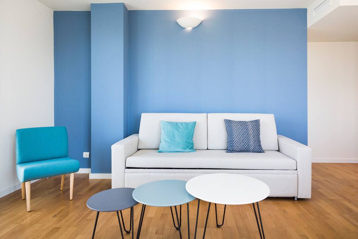 Un salon moderne avec un canapé blanc, deux fauteuils bleus et trois petites tables rondes.