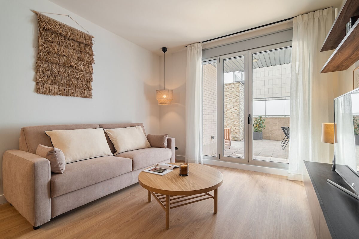 Un salon moderne avec un canapé beige, une table basse ronde en bois et une grande porte-fenêtre coulissante donnant sur un espace extérieur.