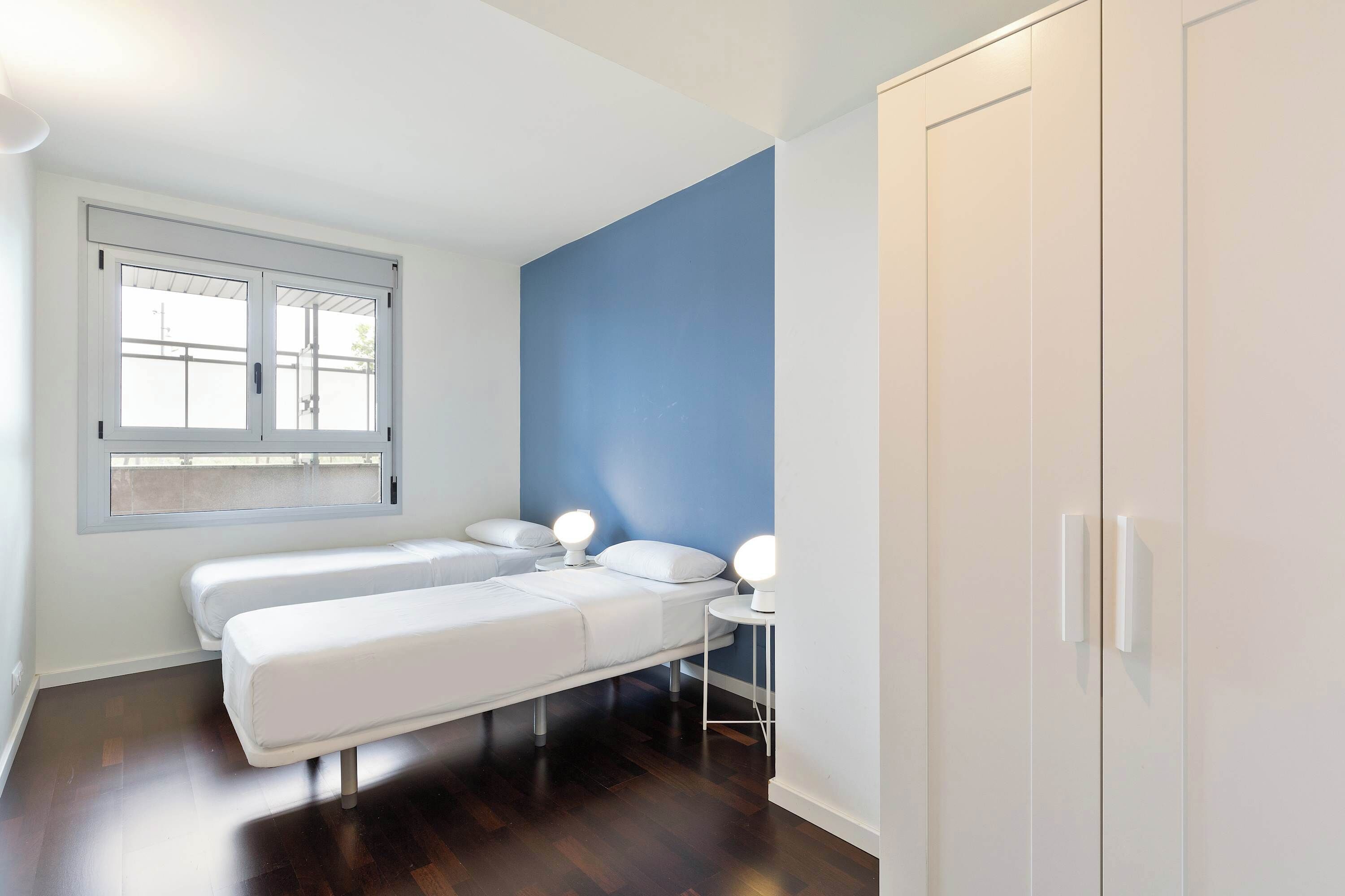 Habitació amb dos llits, una finestra, un armari i làmpades de nit.